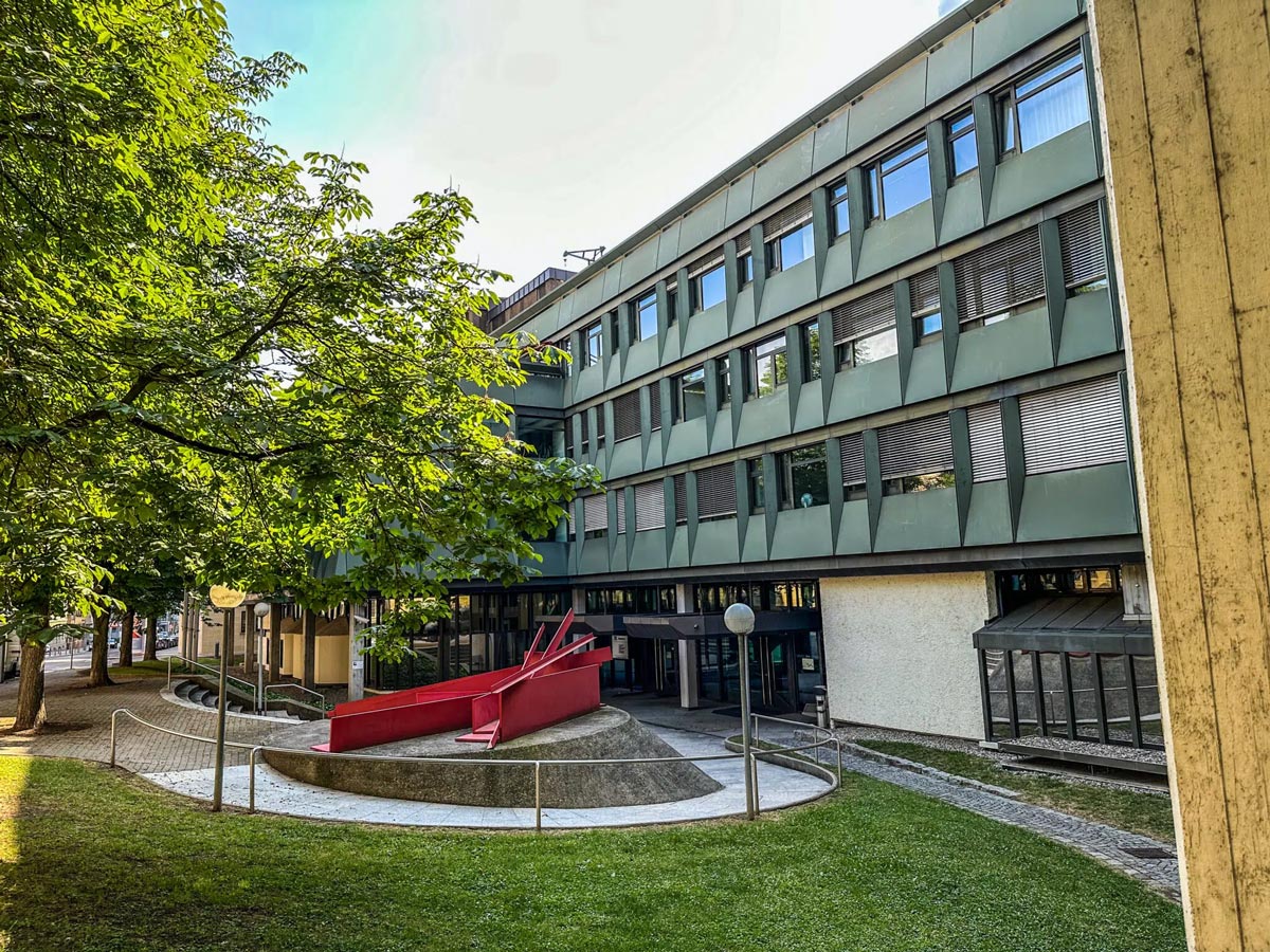 Modern graues Gebäude mit vielen Fenstern und roter Skulptur im Vordergrund