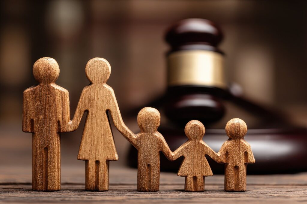 Der Hammer eines Richters sitzt neben hölzernen Familienfiguren, während ein Anwalt den Papierkram vor Gericht erledigt Gerechtigkeit wird in Familiensachen wie Sorgerecht und Scheidung gesucht